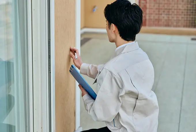作業着姿の男性が外壁にメモを取りながら点検作業をしている様子